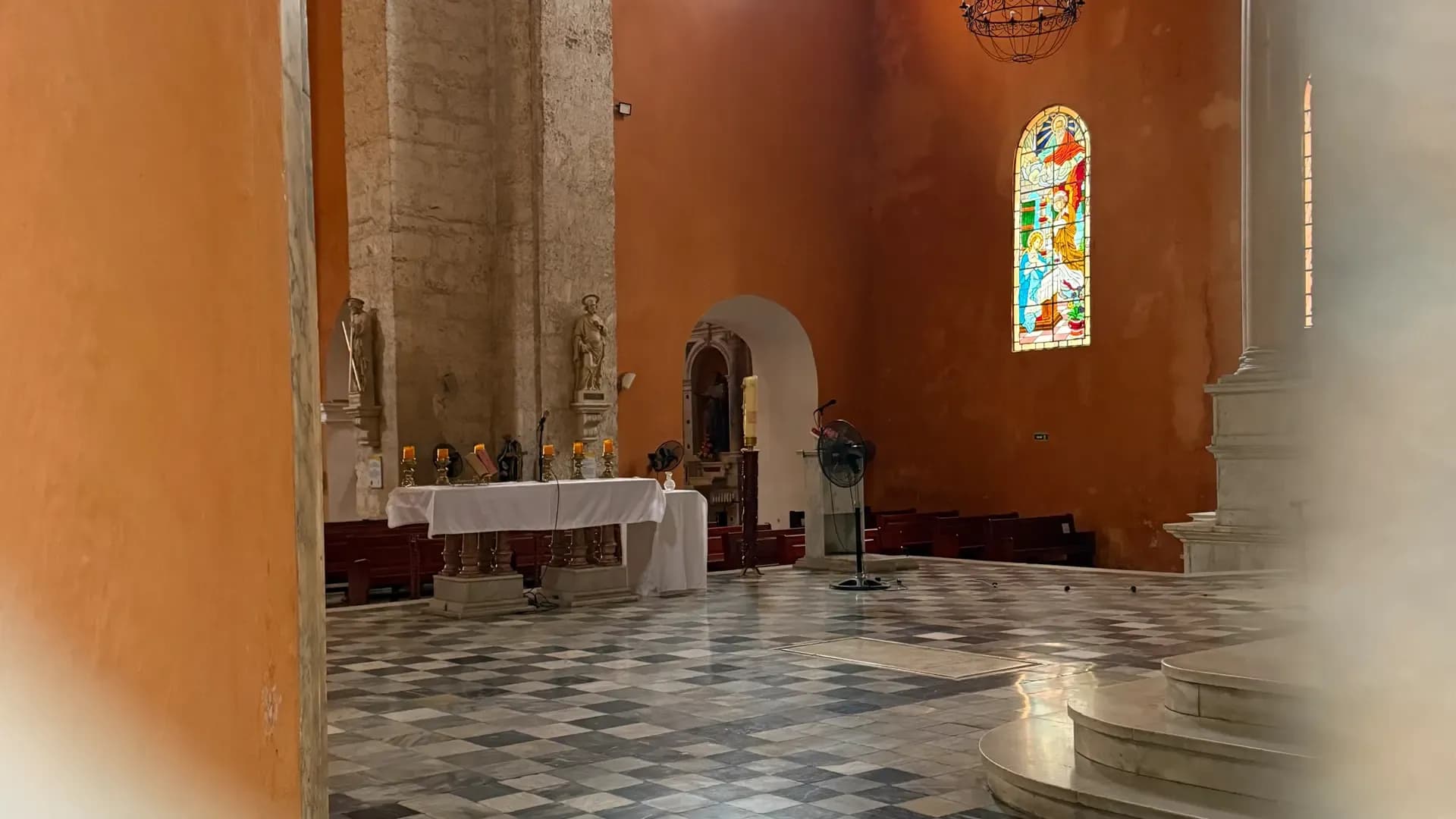 Interior de iglesia colonial con paredes terracota, columnas de piedra, vitral y piso ajedrezado