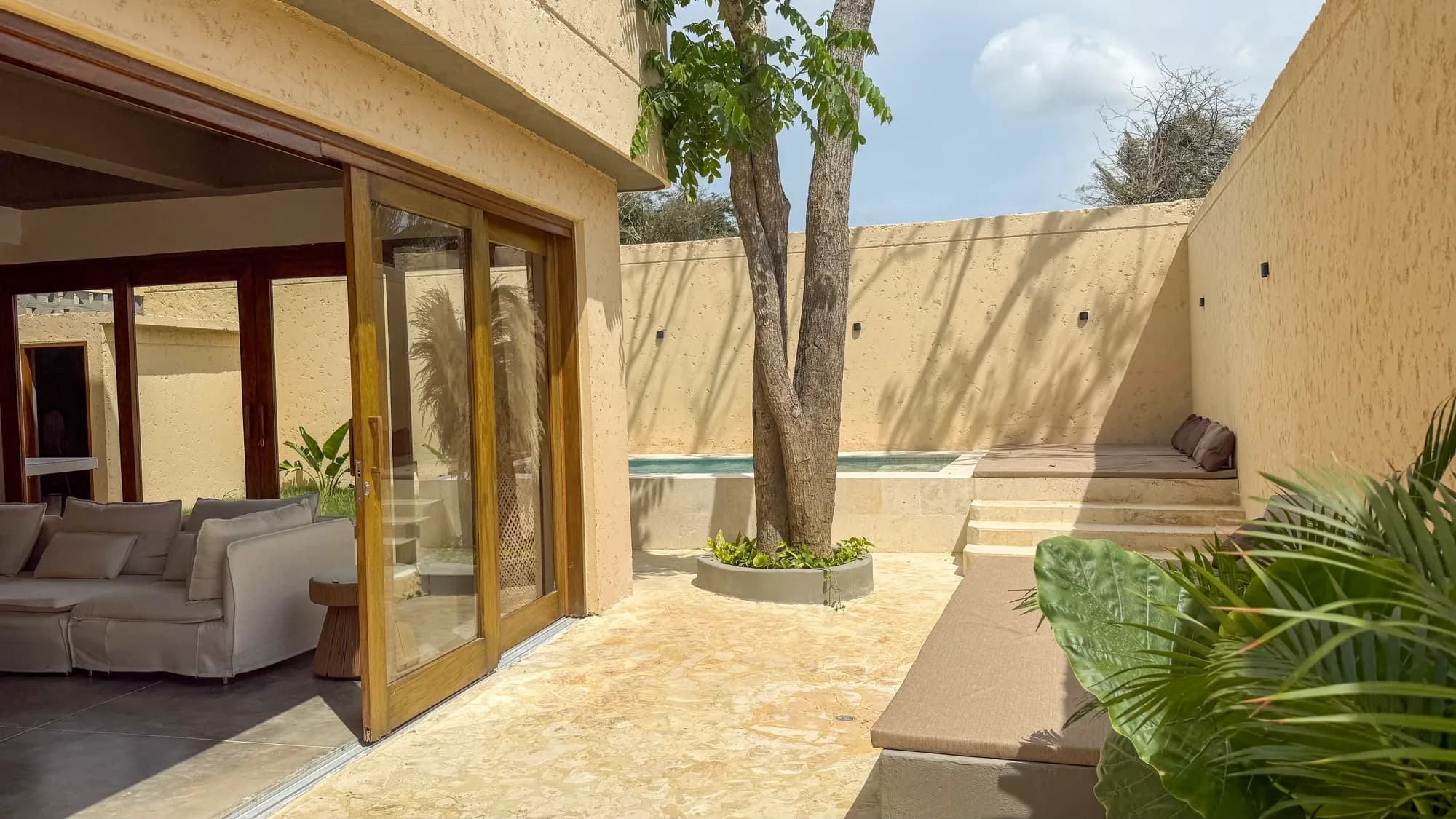 Fachada de dos pisos color arena con muro decorativo de calados, puerta de madera y pequeno jardin