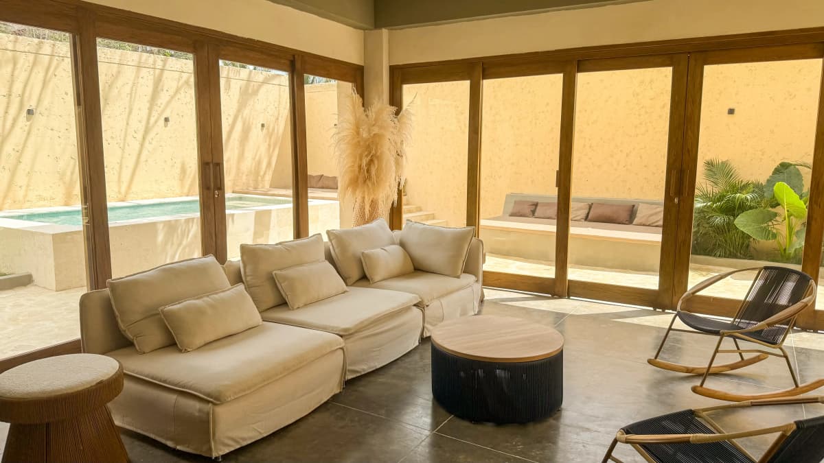 Sala con puertas corredizas abiertas al patio con piscina y plantas tropicales