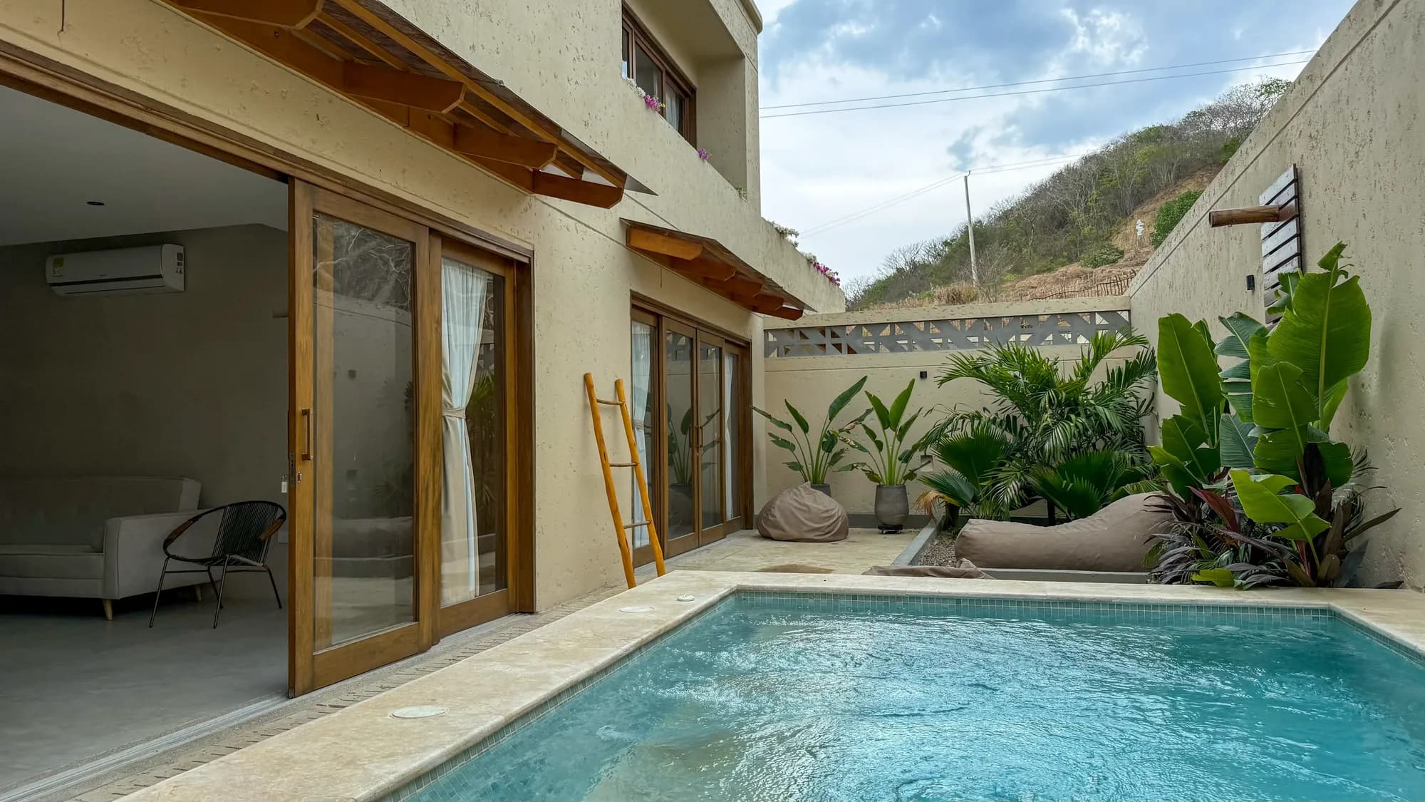 Sendero de entrada renderizado entre casas de dos pisos en tonos tierra con palmeras y jardines tropicales