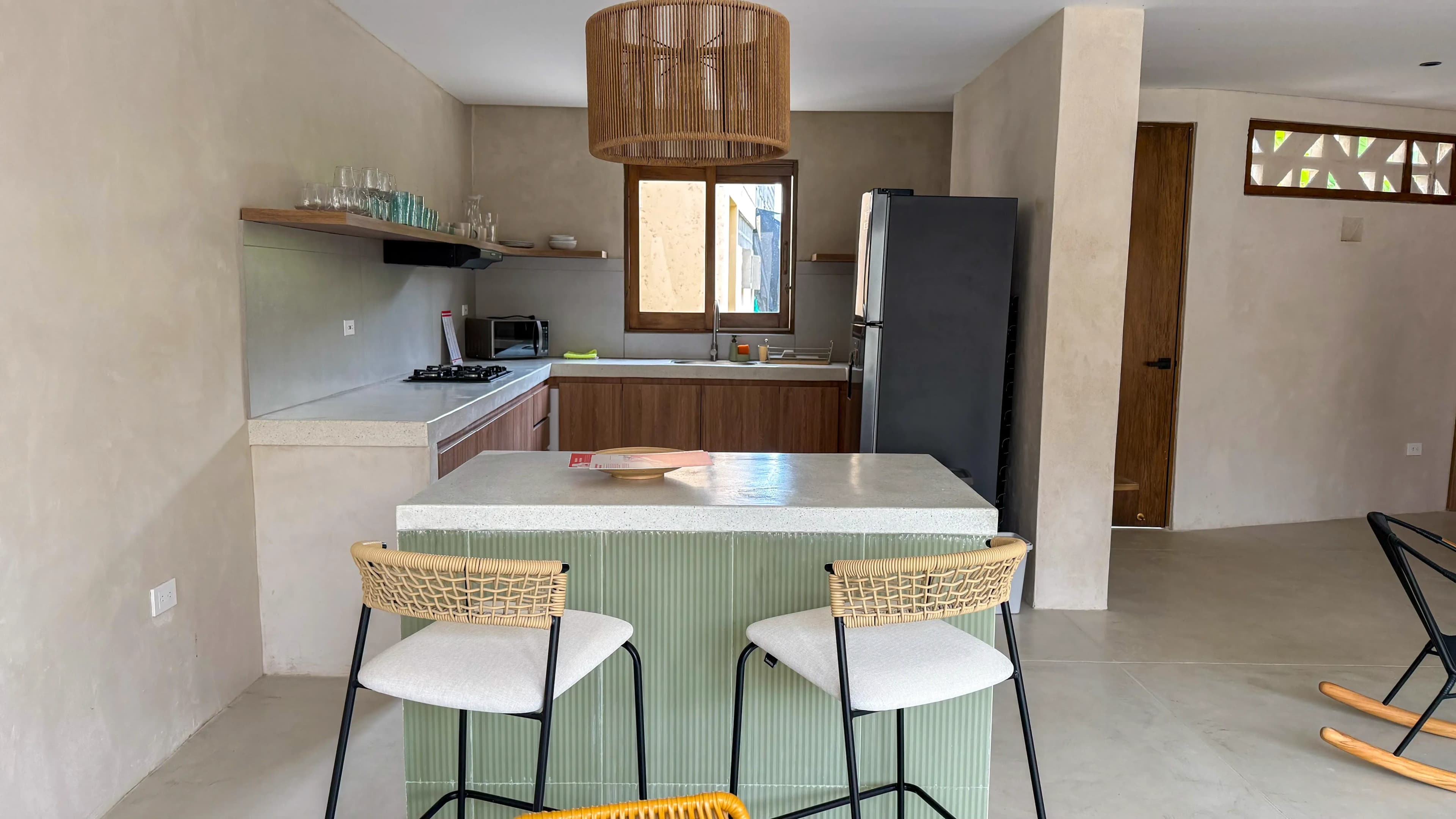 Cocina con isla de azulejos verdes, taburetes de madera y estanteria abierta