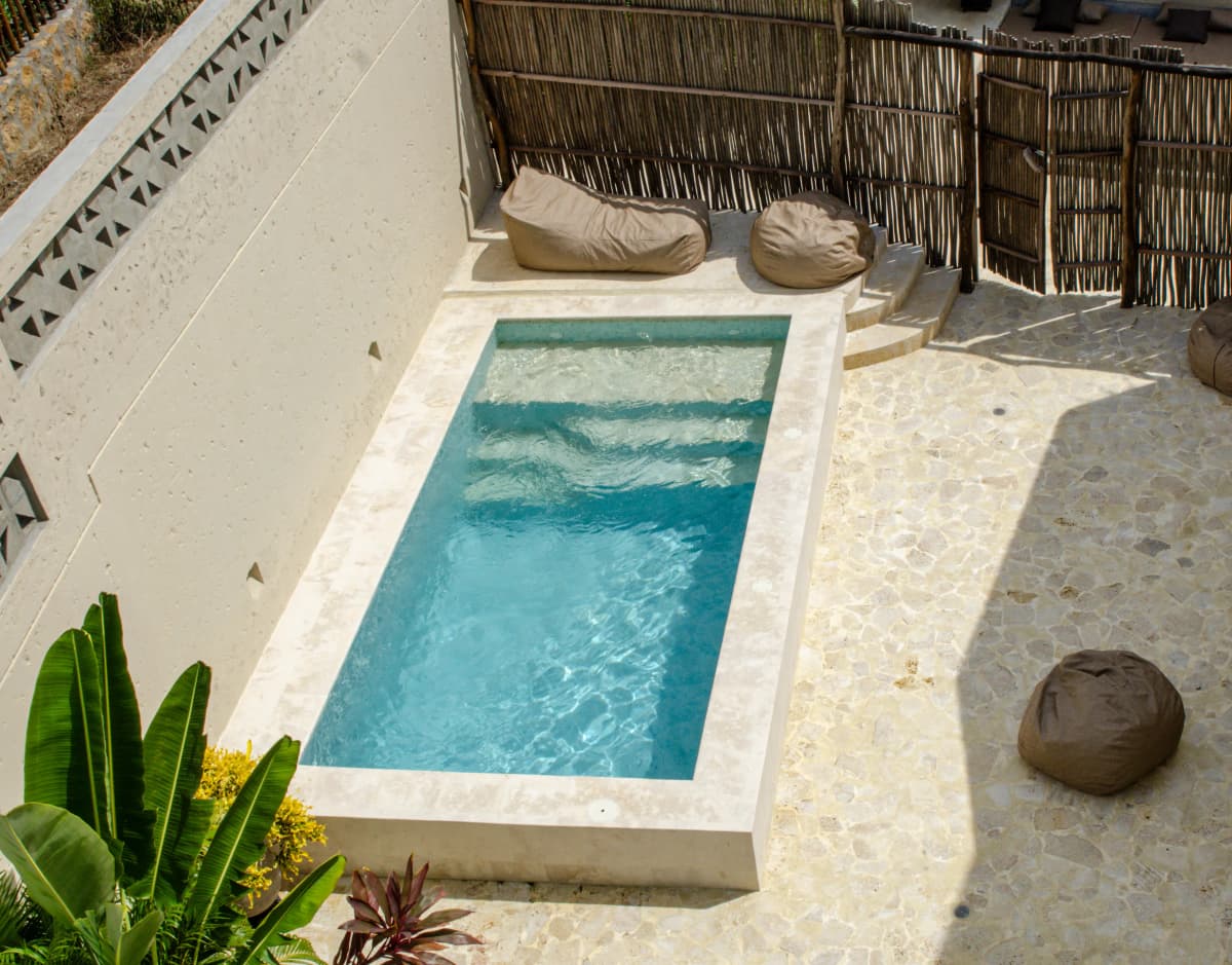 Vista a traves de ventanales de piso a techo hacia el patio con piscina, puffs y muros de calados