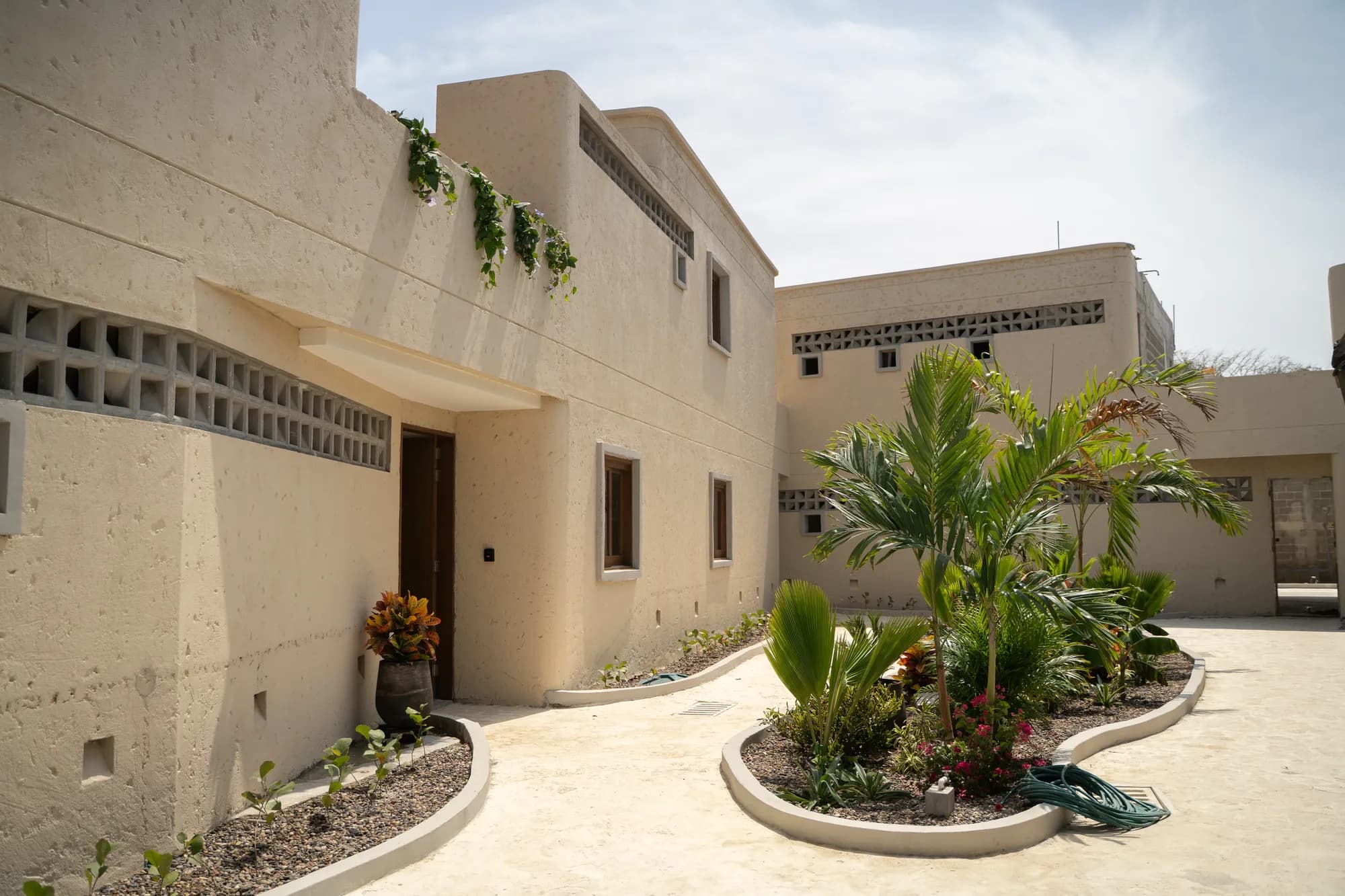 Casa de dos pisos color arena con detalles de calados, jardin tropical y camino curvo de piedra