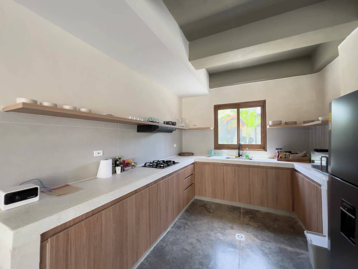 Cocina en L con gabinetes de madera, mesadas de piedra, estante abierto y ventana con vista al jardin