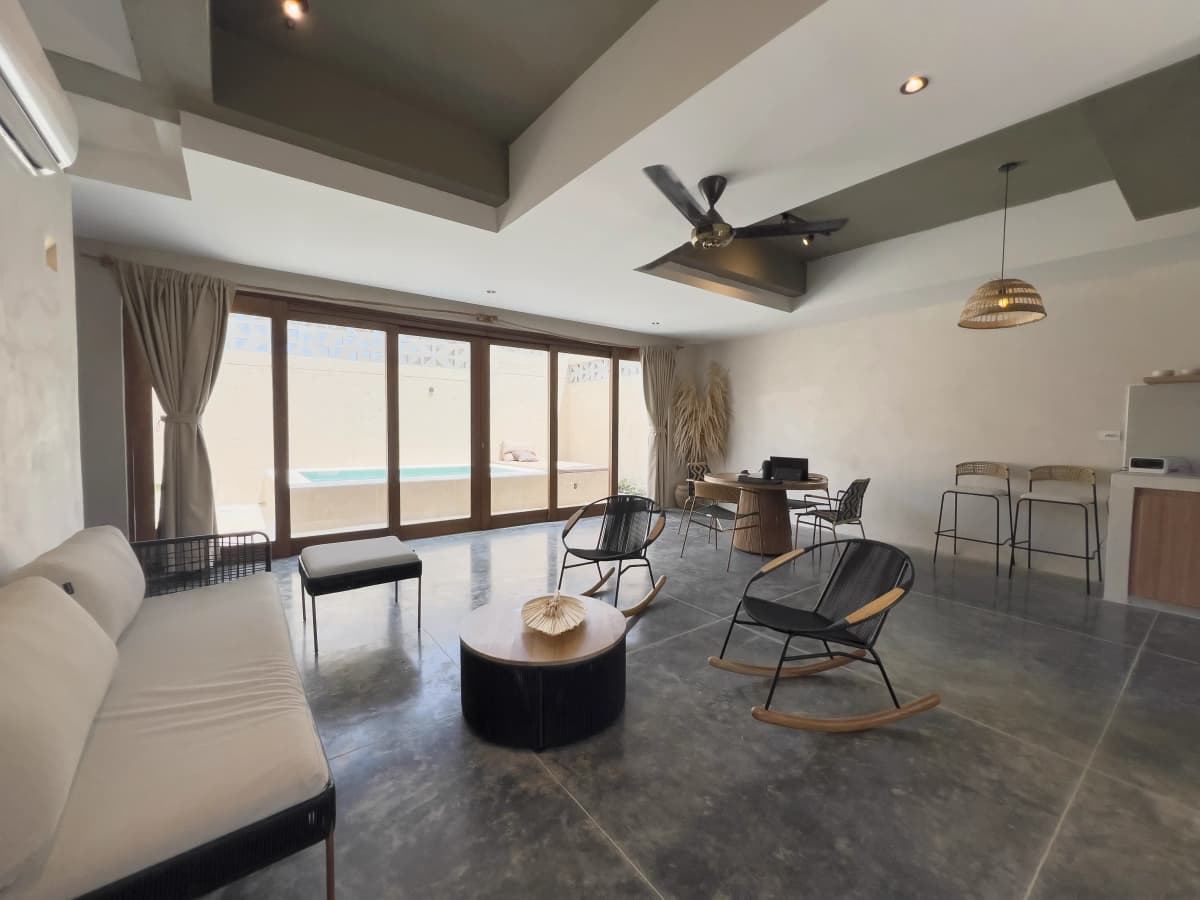 Sala abierta con sofa, mecedoras, taburetes de barra y puertas de vidrio hacia el area de piscina