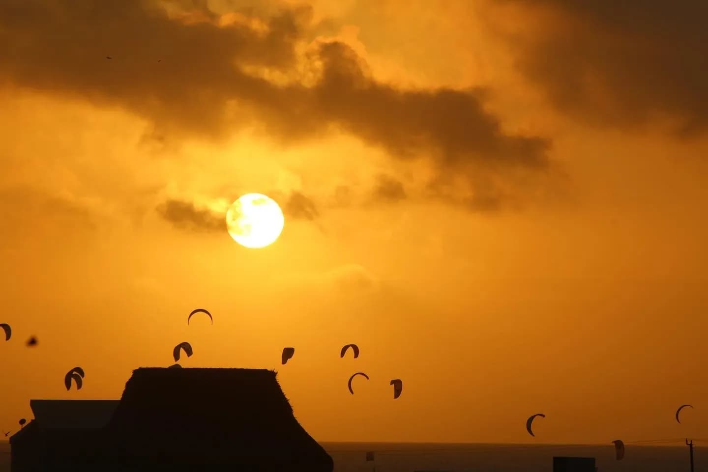 Dramatico atardecer dorado sobre los techos con siluetas de kitesurfistas contra el cielo