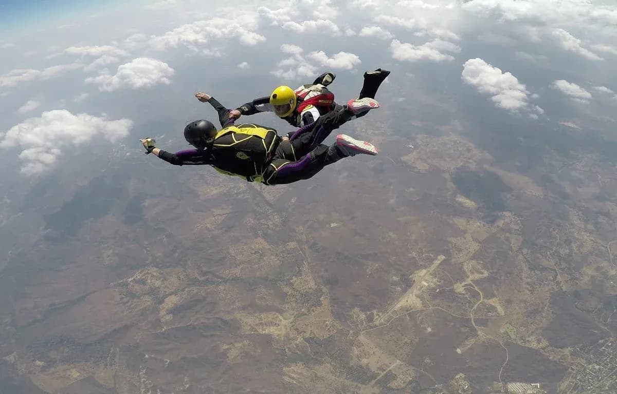 Dos paracaidistas en tandem en caida libre sobre el campo verde colombiano con nubes