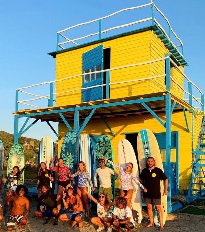 Grupo de surfistas posando con tablas frente a una colorida escuela de surf amarilla y azul
