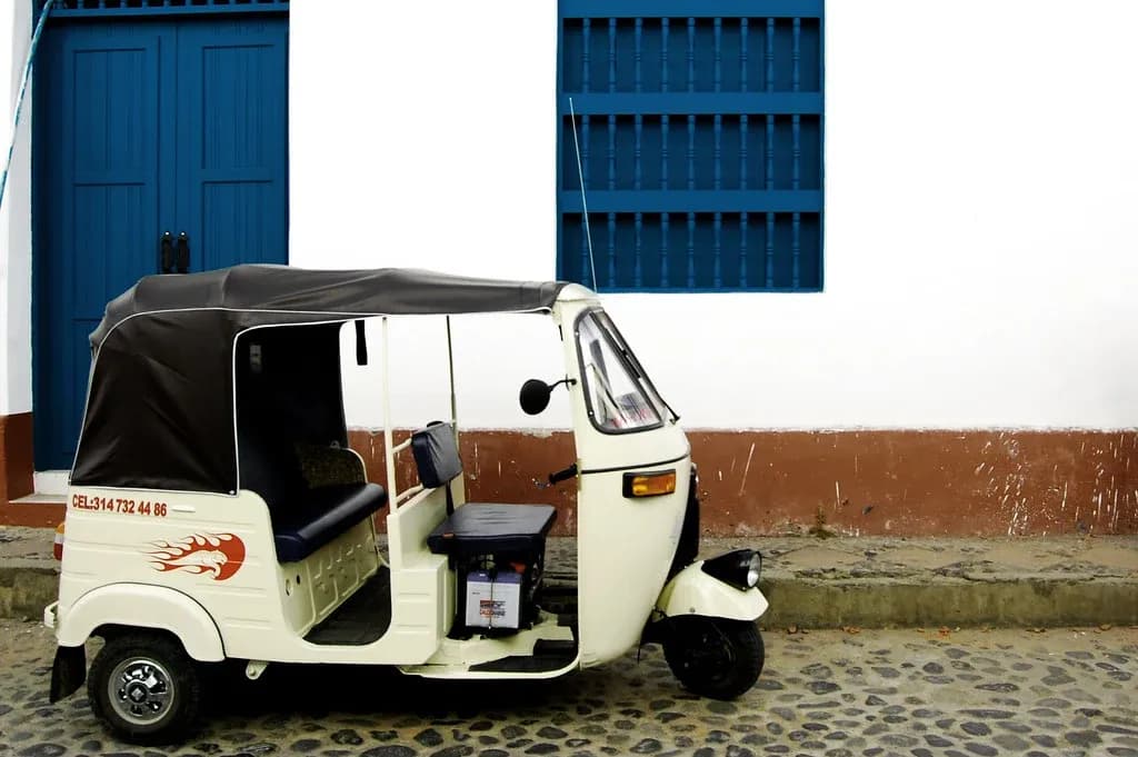 Tuc-tuc blanco de tres ruedas estacionado en calle empedrada frente a puertas coloniales coloridas