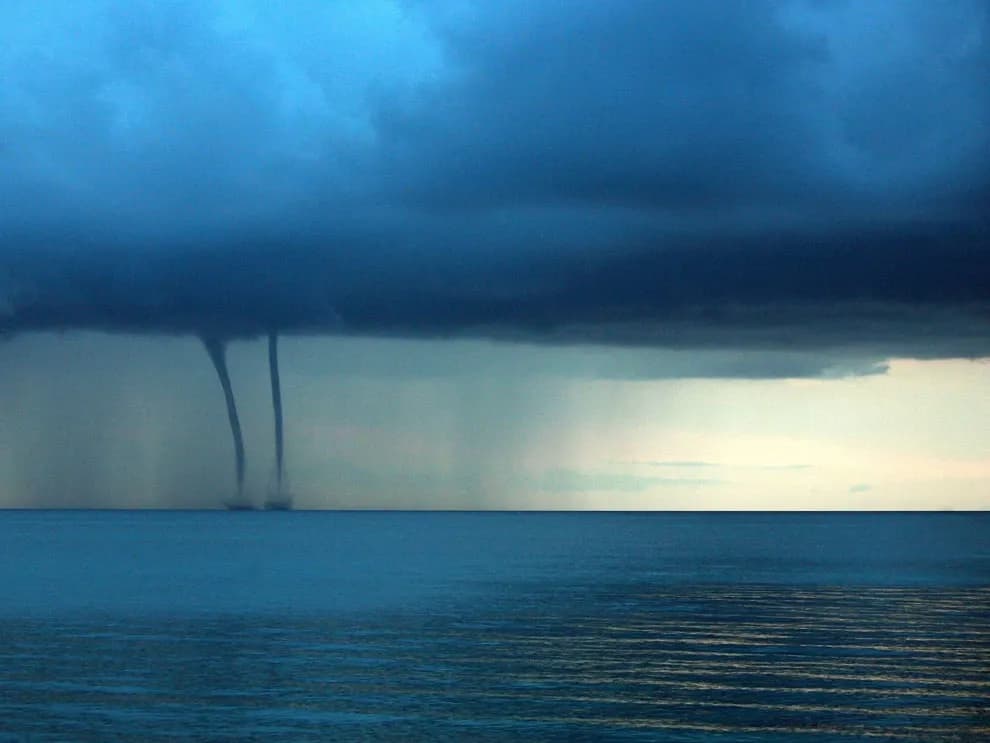 Dos embudos de tromba marina descendiendo de nubes oscuras de tormenta sobre el mar Caribe en calma